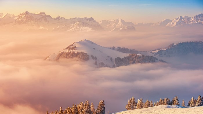 Snowy mountains above clouds at sunrise