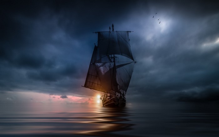 Sailing ship on the sea at sunset with storm clouds