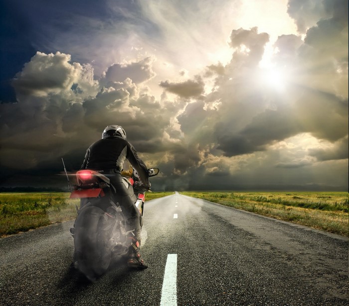 Motorcyclist on a road under stormy clouds