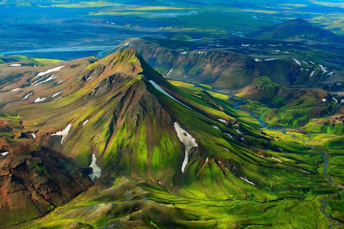Aerial view of a green mountain range with snow patches and a river