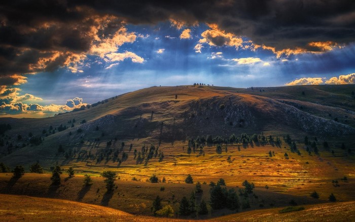Sun rays over a mountain landscape with clouds and trees