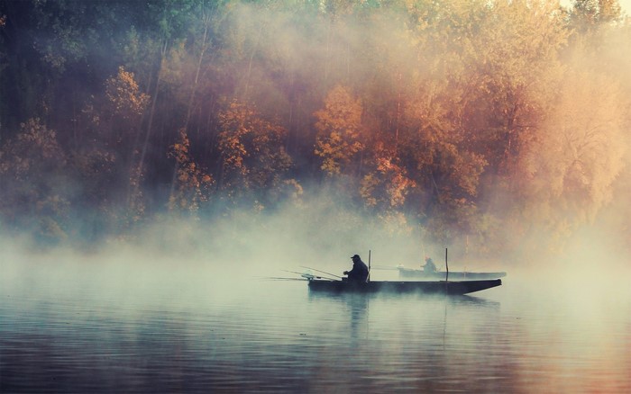 Fishermen in boats on a misty lake at sunrise