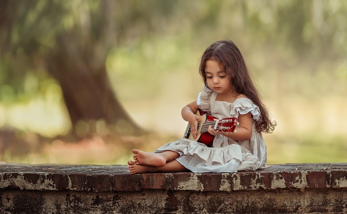 Young girl playing a small guitar outdoors