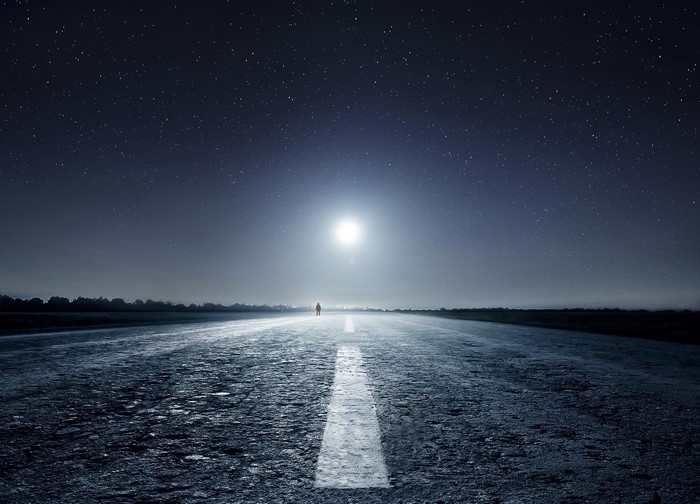 Man standing on a road under a starry night sky with moon