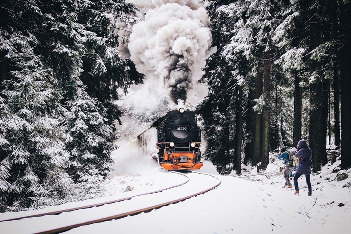 Steam train in a snowy forest with onlookers