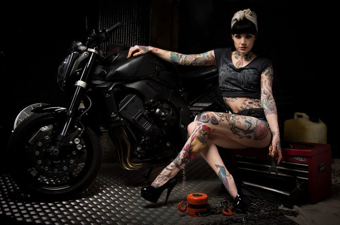 Woman with tattoos sitting on a toolbox next to a motorcycle