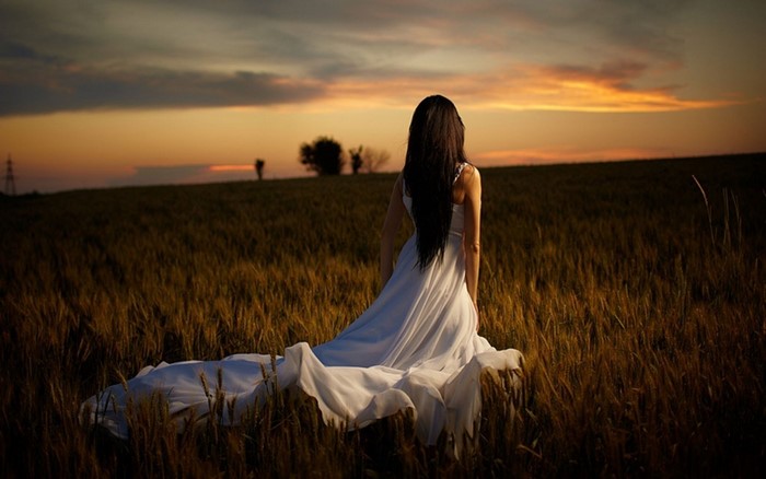 Woman in white dress in a field at sunset