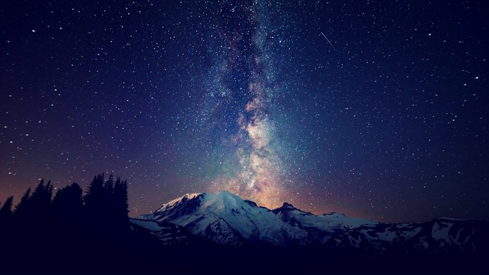 Milky Way over snow-capped mountains and pine trees