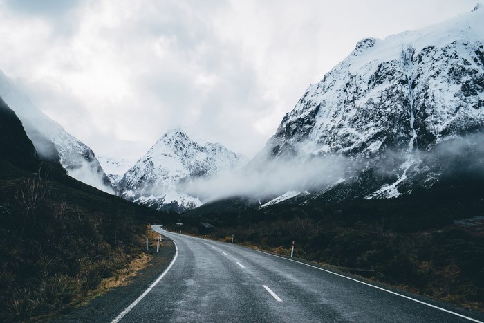 Winding road through snow-capped mountains under cloudy sky