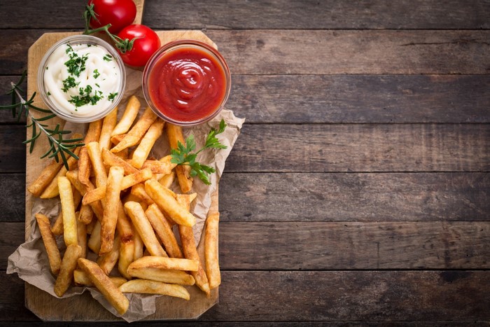French fries with ketchup and mayonnaise on a wooden board