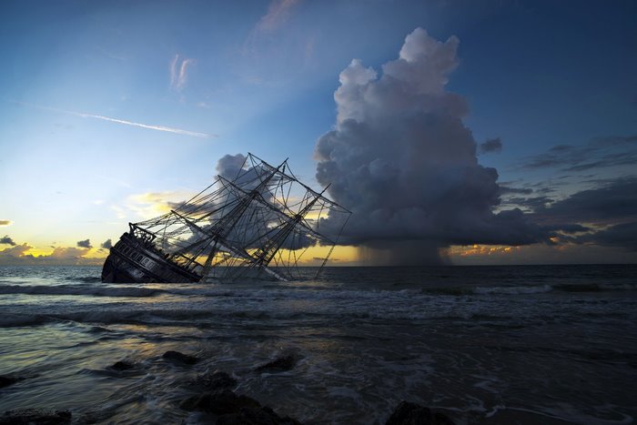 Sinking sailing ship at sunset with storm clouds