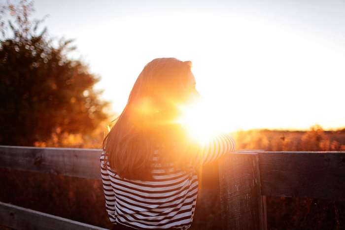 Woman leaning on fence during golden hour sunset
