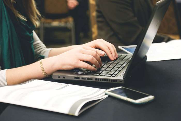 Woman typing on a laptop with a smartphone and papers on a desk