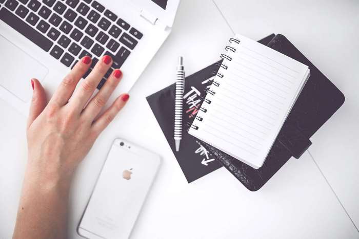 Woman's hand on laptop with iPhone and notebook