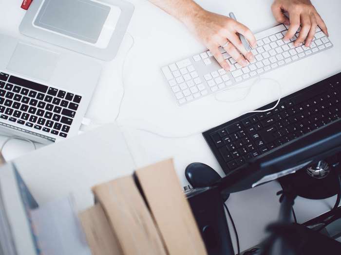 Person typing on keyboards at a desk with laptops