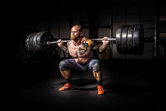 Man performing a heavy barbell squat in a gym 4K