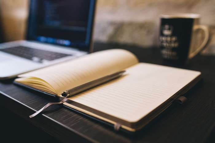 Notebook and pen on a desk with a laptop and mug