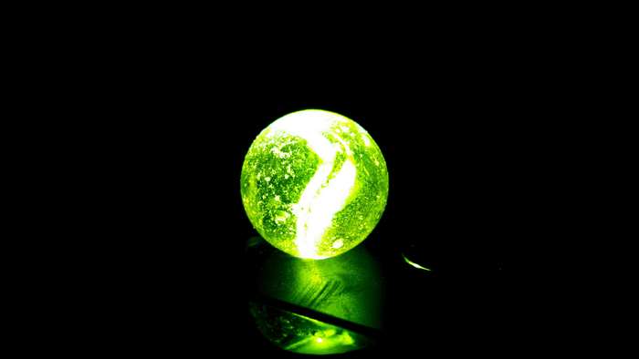 Green glass marble with white swirls on black background