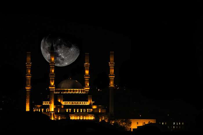 Kocatepe Mosque illuminated at night with a large moon in the sky