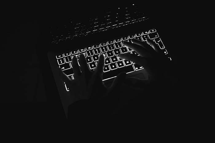 Hands typing on a backlit Apple Macbook Pro keyboard in the dark