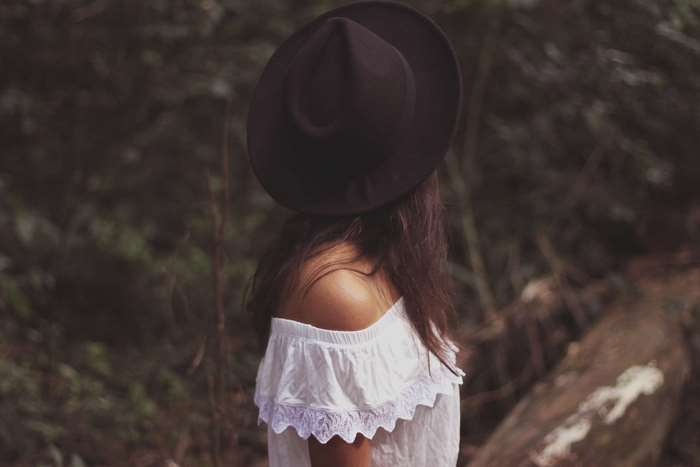 Woman wearing a fedora and off-the-shoulder top in woods