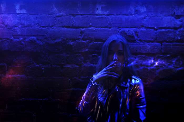Woman smoking in front of a brick wall with neon lights