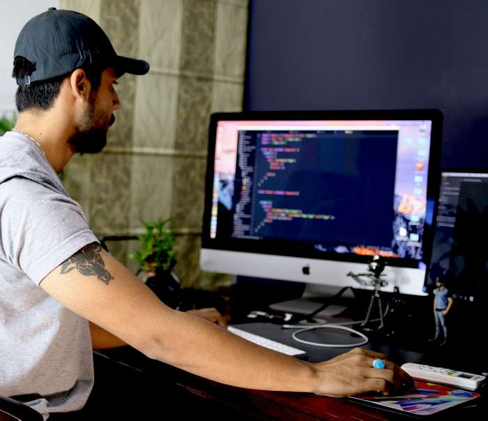 Man wearing a cap coding on an Apple computer