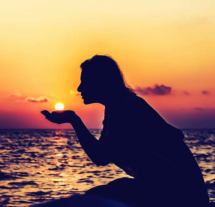 Silhouette of a woman holding the sun at sunset over the ocean