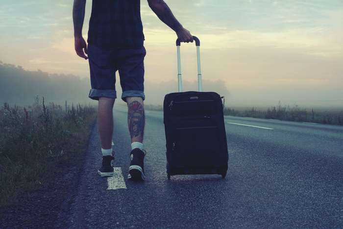 Man with suitcase walking on road at sunrise