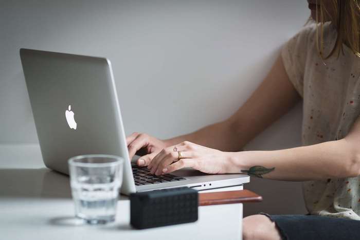 Woman typing on a MacBook laptop with a glass of water