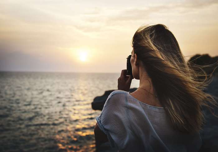 Woman taking photo of sunset over the ocean