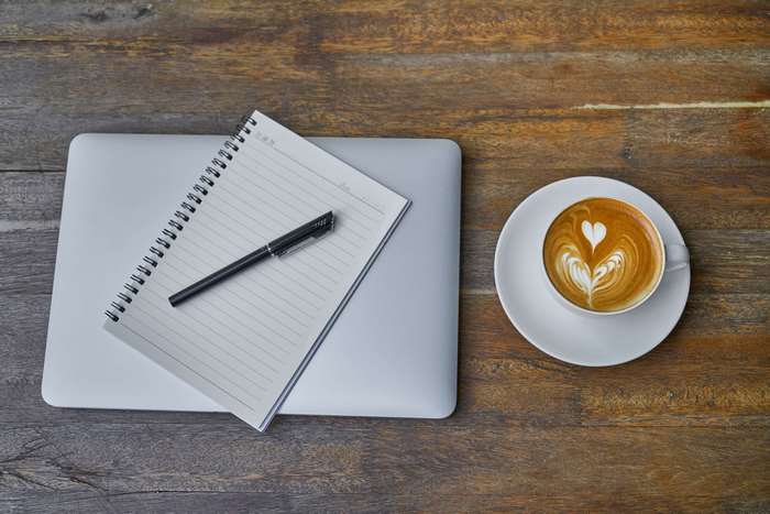 Laptop, notebook, pen, and latte on a wooden table