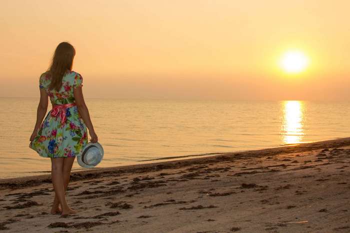 Girl in floral dress holding hat at sunset on beach