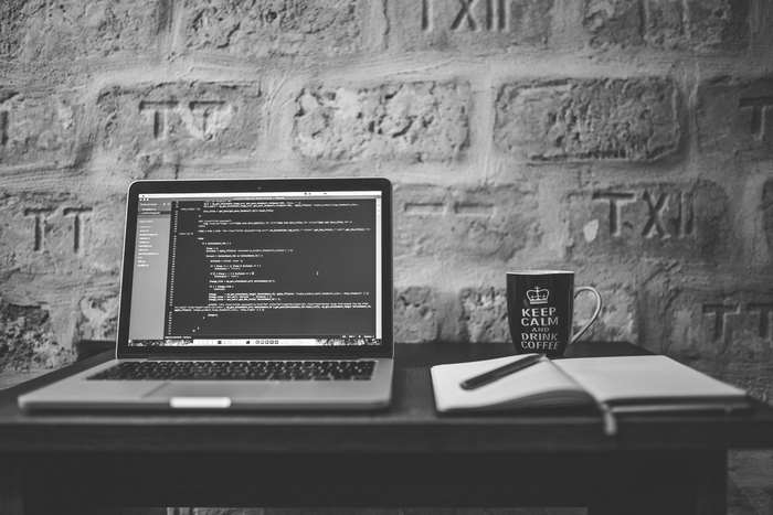 MacBook Pro with code, mug, and notebook on table