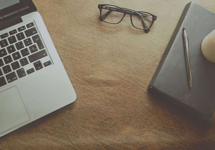 MacBook, eyeglasses, notebook, and pen on leather surface