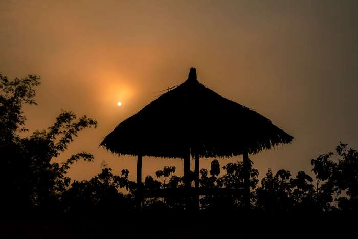 Silhouette of a thatched hut against a sunset