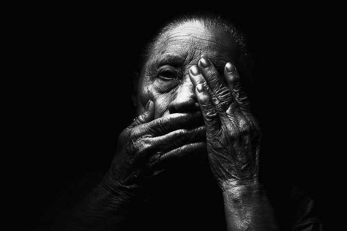 Black and white portrait of an elderly woman covering her face