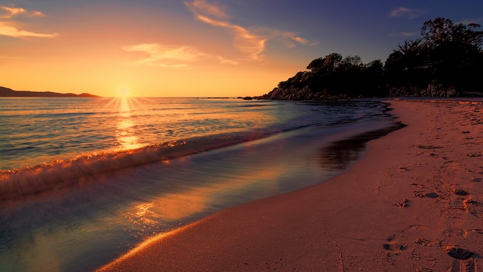 Sunset over the sea with a beach and mountains