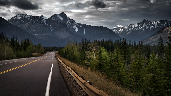 Road leading to snow-capped mountains under cloudy sky