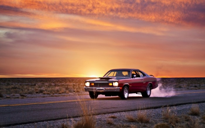 Red muscle car doing a burnout at sunset