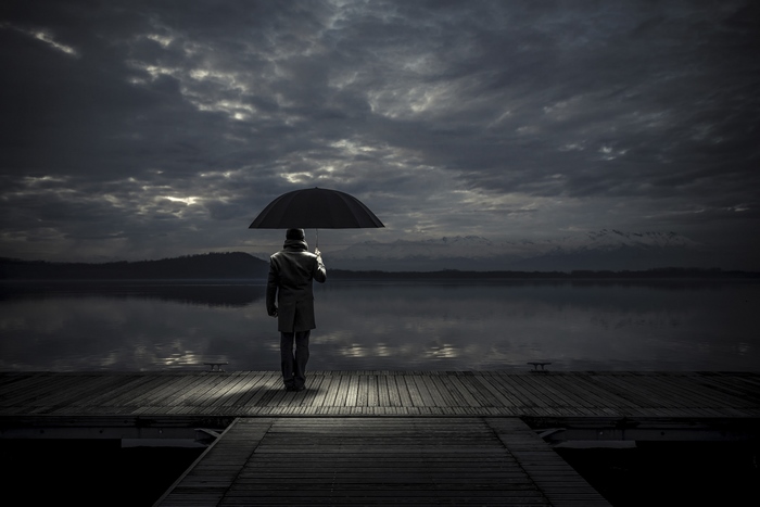 Man with umbrella on a pier by a lake