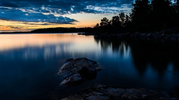 Sunset over a calm lake with trees and rocks