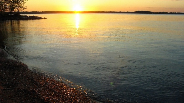 Sunset over a calm lake with a rocky shore