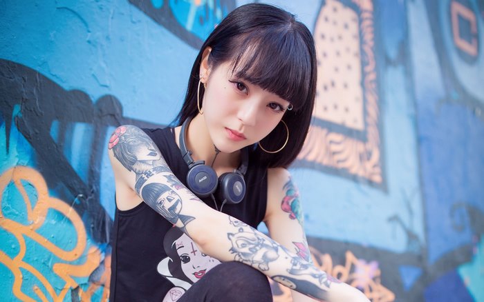 Tattooed Asian woman with headphones and hoop earrings