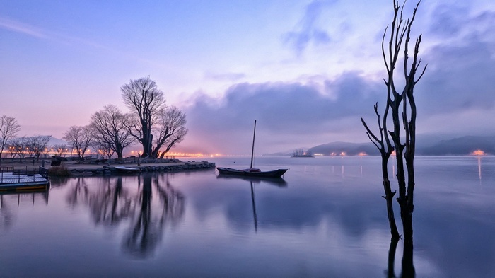 Boat on a calm lake at dawn with bare trees