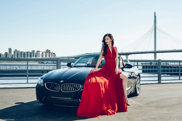 Woman in red dress posing with black BMW