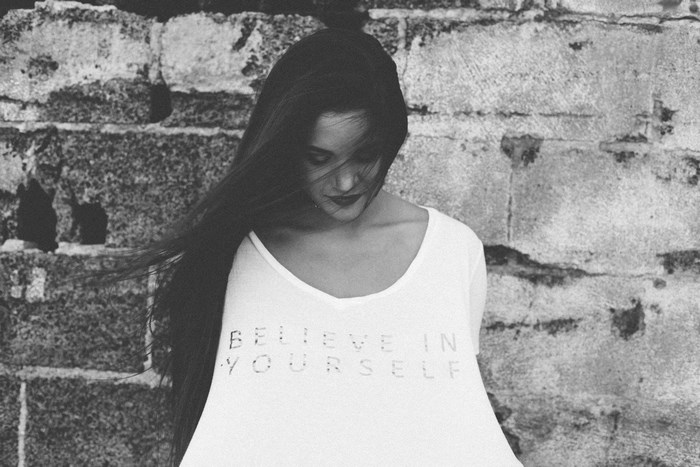 Girl in white t-shirt with text in front of brick wall