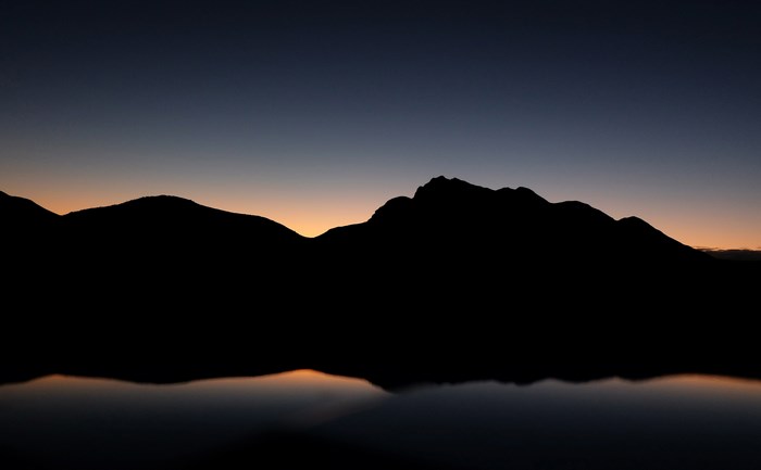 Silhouette of mountains reflected in water at dusk