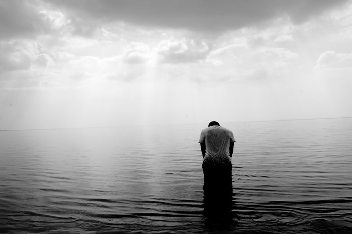 Man in wet shirt standing in water under cloudy sky