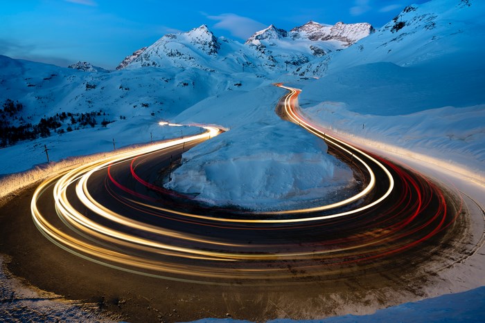 Winding mountain road with car light trails in snow